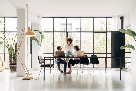 Diverse teamwork brainstorming on a creative project in spacious coworking loft space. Big windows. Multiracial. Startup concept. Coworking space concept. Copy space.