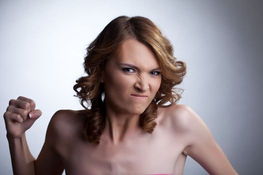 Studio portrait of emotional aggressive young woman with fist