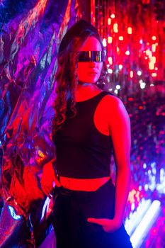 Close-up portrait of caucasian woman in sunglasses in neon light against foil wall