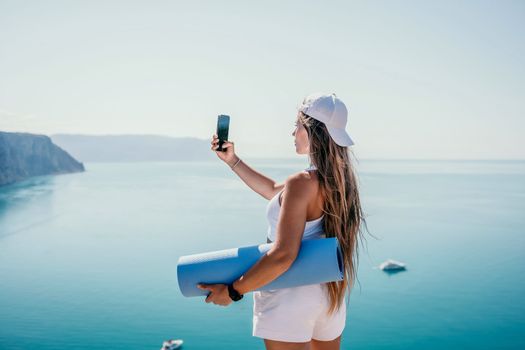 Young woman with black hair, fitness instructor in pink sports leggings and tops, doing pilates on yoga mat with magic pilates ring by the sea on the beach. Female fitness daily yoga concept