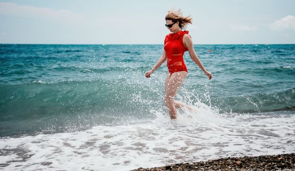 Young happy woman walks carefree on the seaside. Happy lady in red bikini. Portrait beautiful young woman relax smile around beach sea ocean in holiday vacation travel trip.