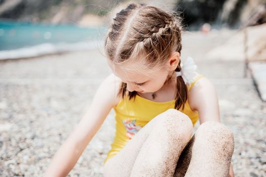 Cute little girl running along the seashore against a clear blue sea and rejoices in the rays of the summer sun. Beautiful girl in yellow swimsuit running and having fun on tropical beach