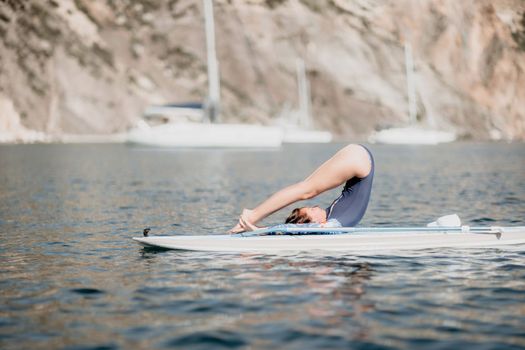 Woman sup yoga. Middle age sporty woman practising yoga pilates on paddle sup surfboard. Female stretching doing workout on sea water. Modern individual hipster outdoor summer sport activity