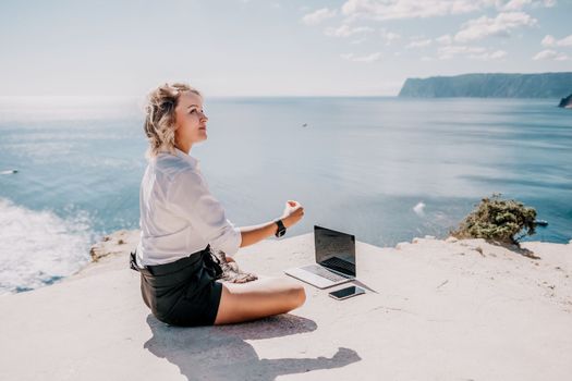 Happy girl doing yoga with laptop working at the beach. beautiful and calm business woman sitting with a laptop in a summer cafe in the lotus position meditating and relaxing. freelance girl remote work beach paradise