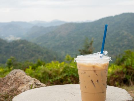 A glass of iced coffee is placed on a rock against a background of mountains and sky.