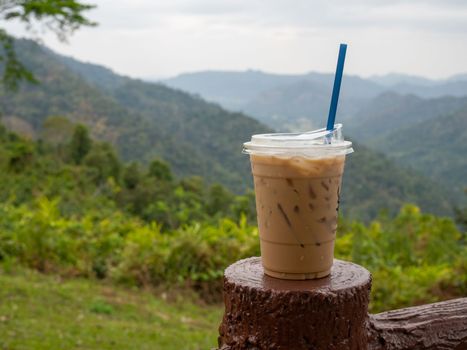 A glass of iced coffee is placed on a rock against a background of mountains and sky.