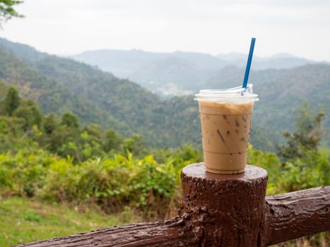 A glass of iced coffee is placed on the fence against a backdrop of mountains and sky.