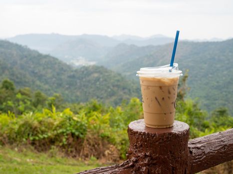 A glass of iced coffee is placed on the fence against a backdrop of mountains and sky.