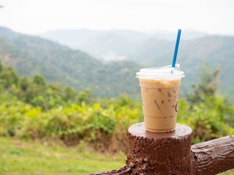 A glass of iced coffee is placed on the fence against a backdrop of mountains and sky.