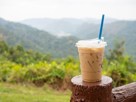 A glass of iced coffee is placed on the fence against a backdrop of mountains and sky.