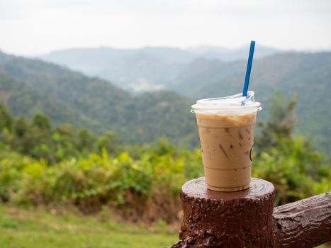 A glass of iced coffee is placed on the fence against a backdrop of mountains and sky.