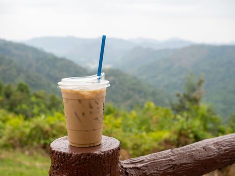 A glass of iced coffee is placed on the fence against a backdrop of mountains and sky.