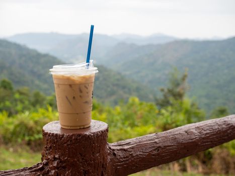 A glass of iced coffee is placed on the fence against a backdrop of mountains and sky.