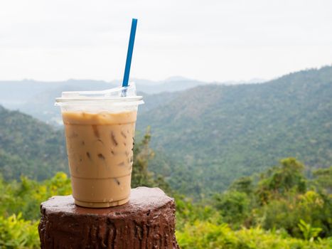 A glass of iced coffee is placed on the fence against a backdrop of mountains and sky.