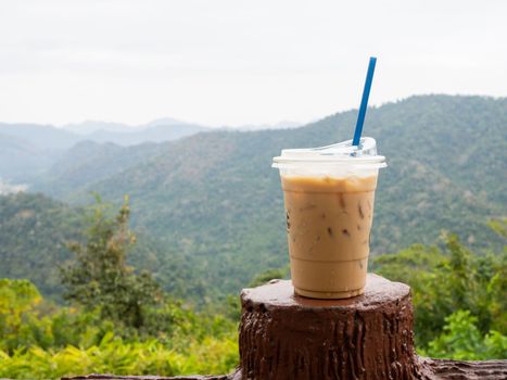 A glass of iced coffee is placed on the fence against a backdrop of mountains and sky.