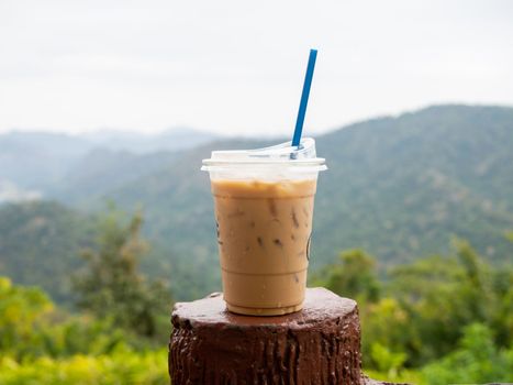 A glass of iced coffee is placed on the fence against a backdrop of mountains and sky.