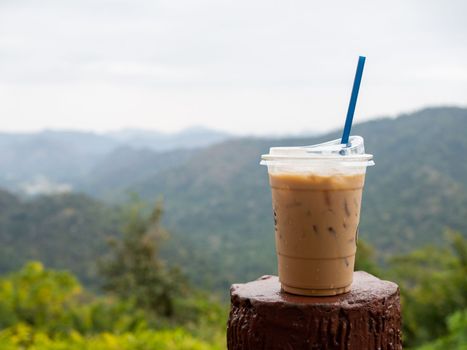 A glass of iced coffee is placed on the fence against a backdrop of mountains and sky.