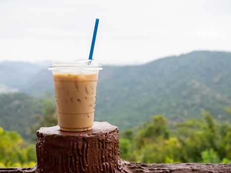 A glass of iced coffee is placed on the fence against a backdrop of mountains and sky.