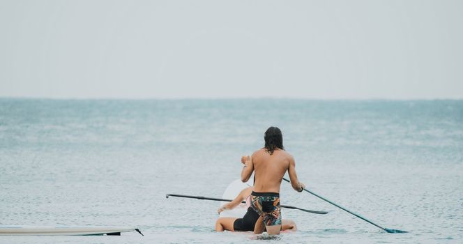 Sea woman and man on sup. Silhouette of happy young woman and man, surfing on SUP board, confident paddling through water surface. Idyllic sunset. Active lifestyle at sea or river