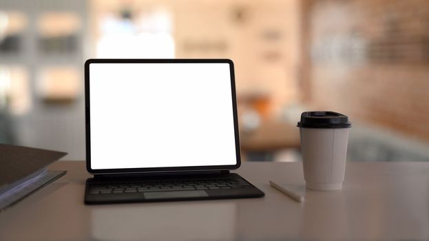 Computer tablet with blank display and coffee cup on white table.