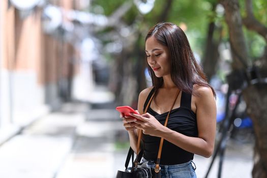 Young cheerful woman standing on the city street and using smart phone.
