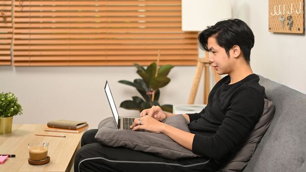 Casual man sitting in living room and browsing internet with laptop computer.
