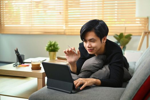 Young Asian man having video call with computer tablet on sofa.