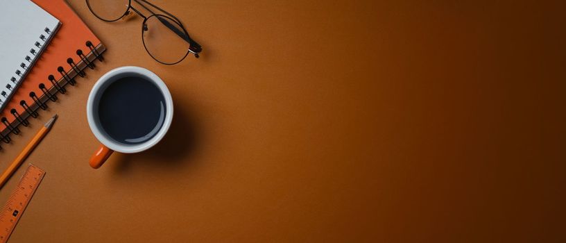 A coffee cup, glasses and notebook on orange leather with cop space.