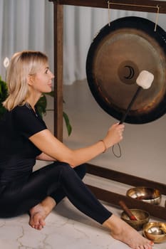 A woman knocks a mallet with a hammer on a gong. A gong and a hand beater for the gong.
