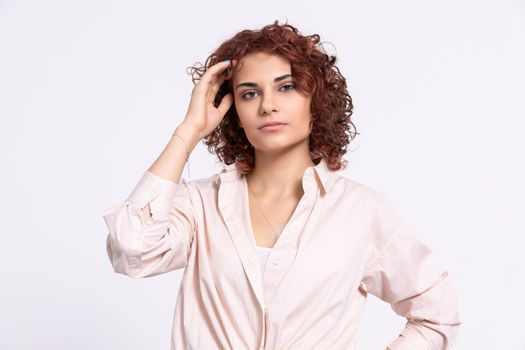 A young girl with short curly chestnut-colored hair. Hand carried up to head height. Light-colored long-sleeved blouse.