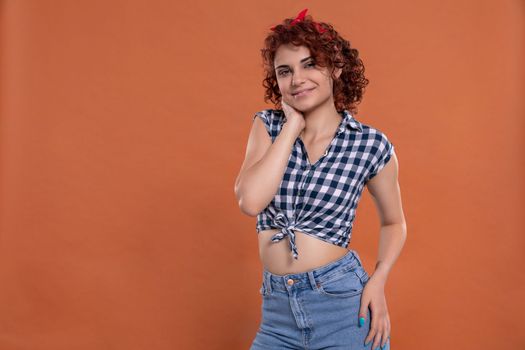 Pin up styling. Girl wearing plaid shirt and tied at the bottom. Short curly hair in chestnut color. Isolated from the uniform background.