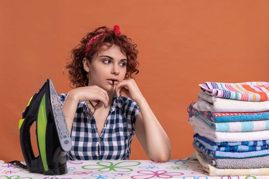 A young woman with glasses and curly hair glances at the work being done. Ironing towels on an ironing board. Isolated from the background.