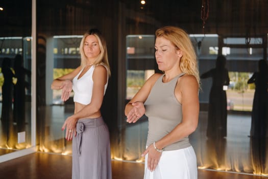 Two beautiful women are doing yoga standing up in the fitness room.