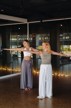 Two beautiful women are doing yoga standing up in the fitness room.