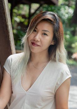 Portrait of gorgeous young woman long blond and white hair in cream dress at wooden house terrace. Resting leisure concept, Selective focus.