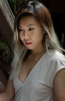 Portrait of young woman long blond and white hair in cream dress at wooden house terrace. Resting leisure concept, Selective focus.