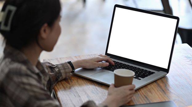 Side view young woman golding coffee cup and using laptop computer.