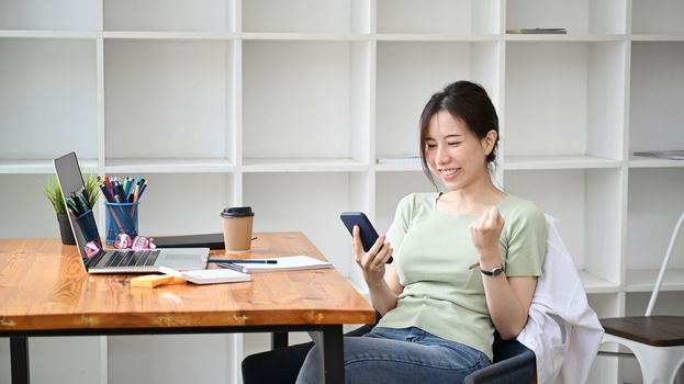 Happy young woman using smartphone and celebrating success.