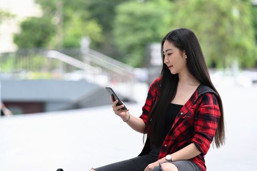 Young woman using smart phone and sitting at outdoors in city.