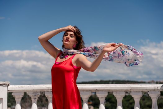 A woman in a red dress against a blue sky and white clouds with a developing scarf around her neck. She turned her face to the wind and posed for the camera