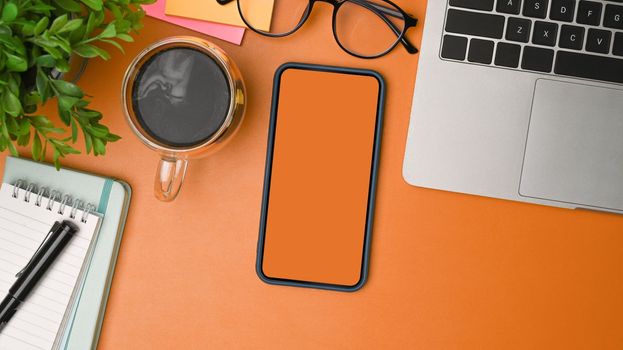 Top view mock up smart phone, coffee cup and computer laptop on orange background.