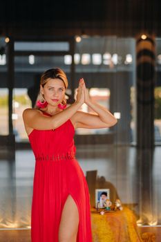 A girl in a red dress moves in a dance meditating indoors . Dynamic dance,