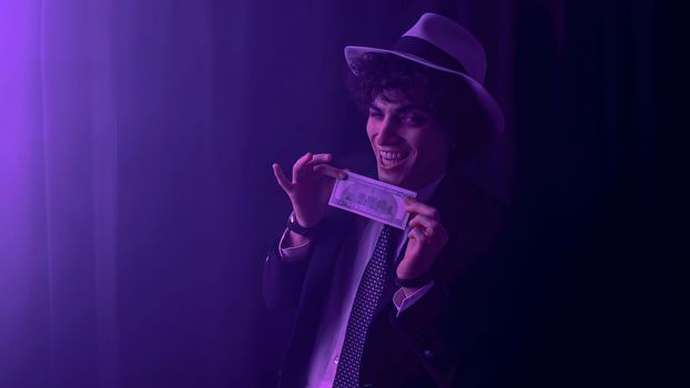 A brunette young man, dressed in a sharp black suit, is seen happily holding a large stack of US dollars. His face is beaming with delight as he counts his earnings.