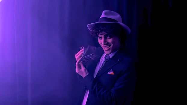 A brunette young man, dressed in a sharp black suit, is seen happily holding a large stack of US dollars. His face is beaming with delight as he counts his earnings.