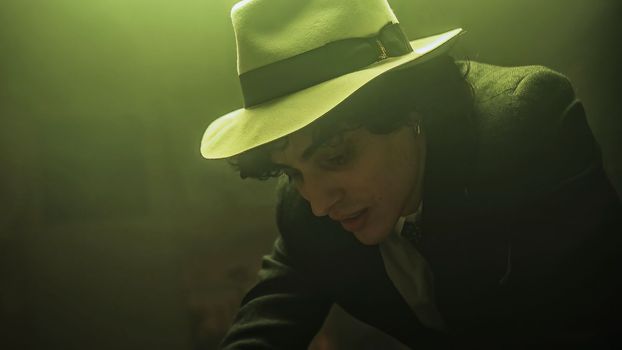 A young man dressed in a black suit and a hat is seen preparing a table for a board game with his friends. The man is focused and ready to play. Spending quality time with friends through board games.