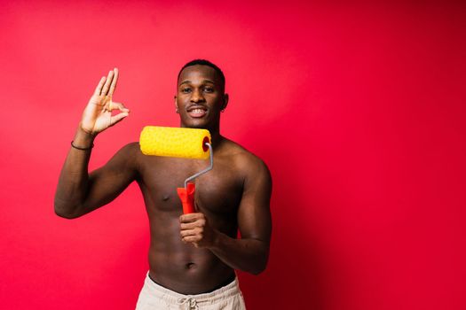 African painter focused on work holding professional roller to paint interior wall, studio.