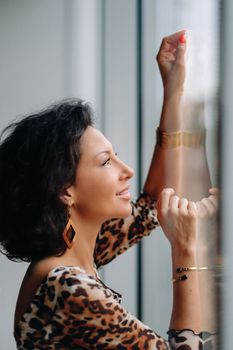 a brunette woman in a tiger dress stands near a large window.