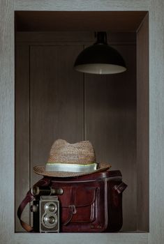 Vintage binocular on Vintage two lens photo camera front of Straw fedora hat on Vintage brown leather bag in Square wooden frame Interior. Vintage style traveling concept, Selective focus.