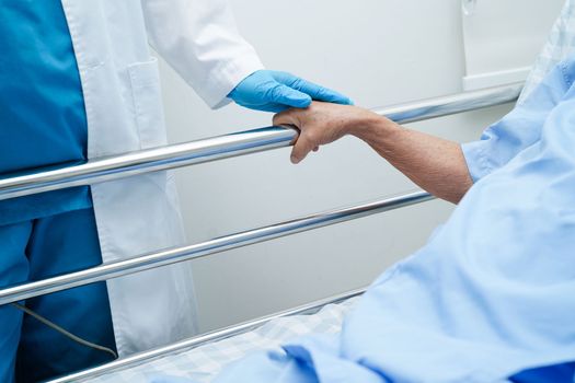 Asian elder senior woman patient holding bed rail while lie down with hope waiting her family in hospital.