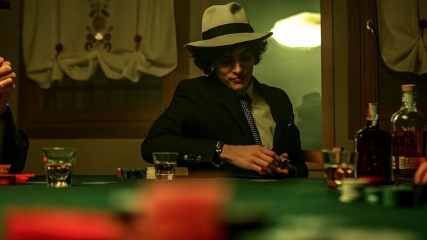 A group of mobsters gather around a table in a dimly lit nightclub. One of them who appears to be the leader of the group is distributing cards among the members to start a game of poker.